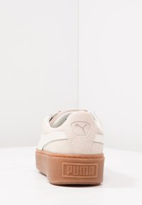 Baskets Puma avec un dessus en suède beige, des accents blancs et une semelle en caoutchouc brun épais. Présente un logo sur le talon et un col rembourré.