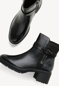 Bottines noires en cuir lisse, ornées d'une sangle décorative et d'un accent en relief de crocodile. Talon bas et fermeture éclair sur le côté.