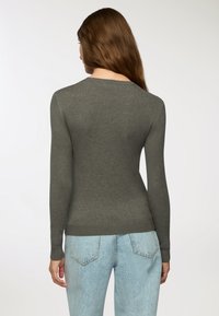 Ciemnozielony, dopasowany sweter z długimi rękawami i okrągłym dekoltem, w połączeniu z jasnoniebieskimi dżinsami. Gładka faktura, minimalne detale.