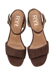 Sandali in suede marrone con una larga fascia frontale, cinturino alla caviglia e tacco a blocco. L'interno presenta lettering dorato. Soletta in pelle liscia.