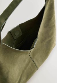 Oliven grøn suede håndtaske med en glat tekstur, der har en sidelukning med knap og et rummeligt indre. Vinklet design og bred strop.