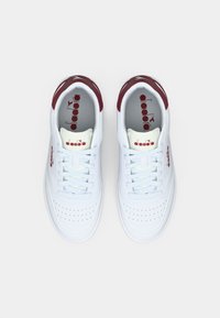 Λευκά δερμάτινα αθλητικά παπούτσια με μαρουντζένιες λεπτομέρειες, επίπεδα λευκά κορδόνια, διάτρητο μπροστινό μέρος και λογότυπο στη γλώσσα και στο πλάι.