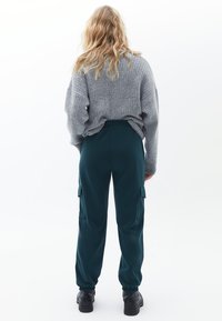 Maglione grigio a coste con maniche ampie abbinato a pantaloni cargo verde scuro con tasche laterali e polsini elasticizzati, indossato con scarpe nere chunky.