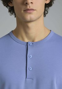 Camicia azzurra con colletto e tre bottoni all'collo, realizzata in un tessuto morbido, caratterizzata da una texture a coste e un design semplice.