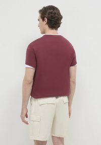 Camicetta corta bordeaux con rifinitura bianca del colletto, texture liscia, vestibilità rilassata. Abbinata a pantaloni cargo beige con tasche laterali.