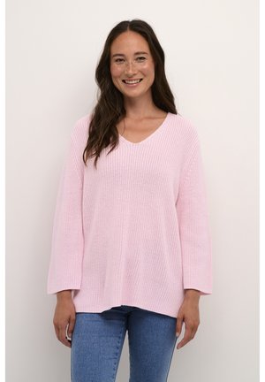 Lichtroze oversized gebreide trui met een V-hals, textuurstof en driekwartmouwen, gecombineerd met blauwe denim jeans.