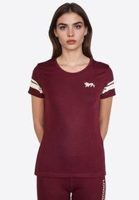 Camiseta burdeos de algodón suave con escote redondo, mangas cortas y acentos de rayas blancas en las mangas. Presenta un logo de león en el pecho.