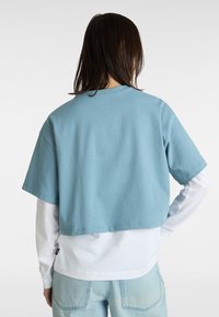 Skåret blå t-shirt lavet af blødt bomuld med korte ærmer, lagt over en langærmet hvid skjorte, parret med lyseblå jeans.