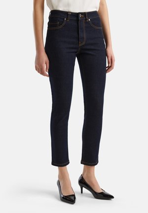 Donkerblauwe high-waisted jeans met contrasterende oranje stiksels, slim fit, enkellengte, gecombineerd met zwarte gepolijste leren pointed heels.