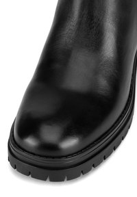 Čierna kožená členková topánka s hladkým povrchom, okrúhlou špičkou, hrubou vonkajšou podrážkou s hlbokým vzorom a viditeľným šitím pozdĺž okraja.