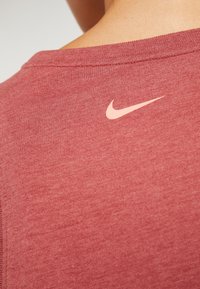 Camiseta de algodón roja con cuello redondo y un pequeño logo de Nike en beige en la parte superior de la espalda. La tela parece suave y ligera.