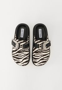 Zebra pattern clogs made of soft material, featuring a black strap and silver buckle. Black soles and cushioned insoles for comfort.
