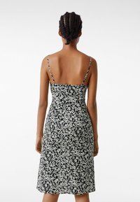 Svart blommig klänning med vita och krämfärgade prästkragar, åtsittande överdel, spagettibandshängslen och knälång nederdel. Slät tygliknande textur.