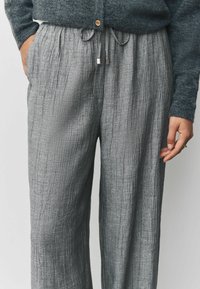 Helle graue weite Hose aus strukturiertem, zerknittertem Stoff. Mit einem elastischen Bund und einem Kordelzug sowie silberfarbigen Hardware-Akzenten.