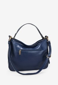 Bolso de piel azul marino con un diseño curvado, que cuenta con un asa superior y una correa de hombro ajustable, además de un bolsillo frontal con cremallera. Accesorios en dorado.