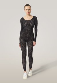 Body en dentelle noire à manches longues, présentant des motifs complexes et une coupe moulante. Porté avec des baskets blanches.