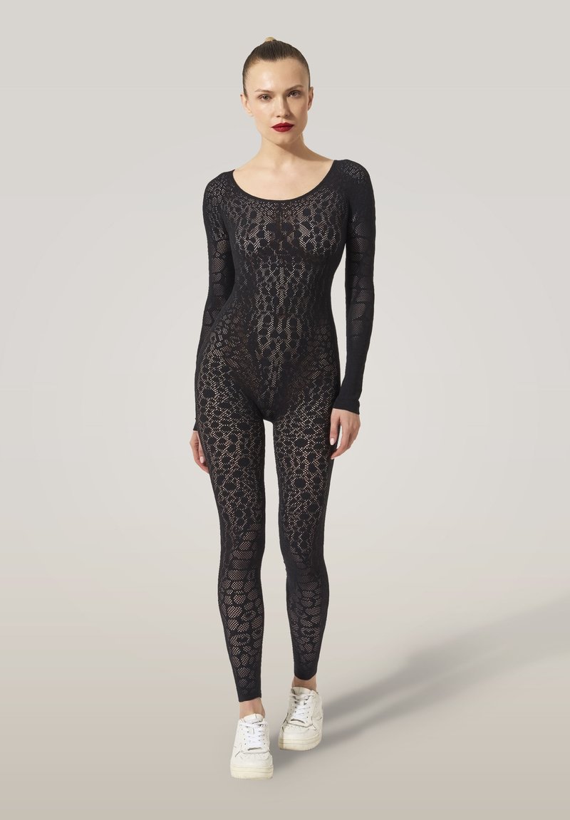 Body en dentelle noire à manches longues, présentant des motifs complexes et une coupe moulante. Porté avec des baskets blanches.