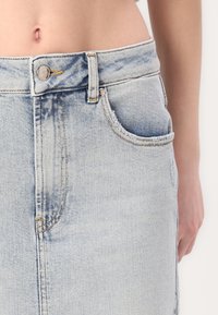 Lyseblå denimskjørt med høy midje, knappestolpe foran og sidelommer. Har slitte kanter og subtil falming for tekstur.