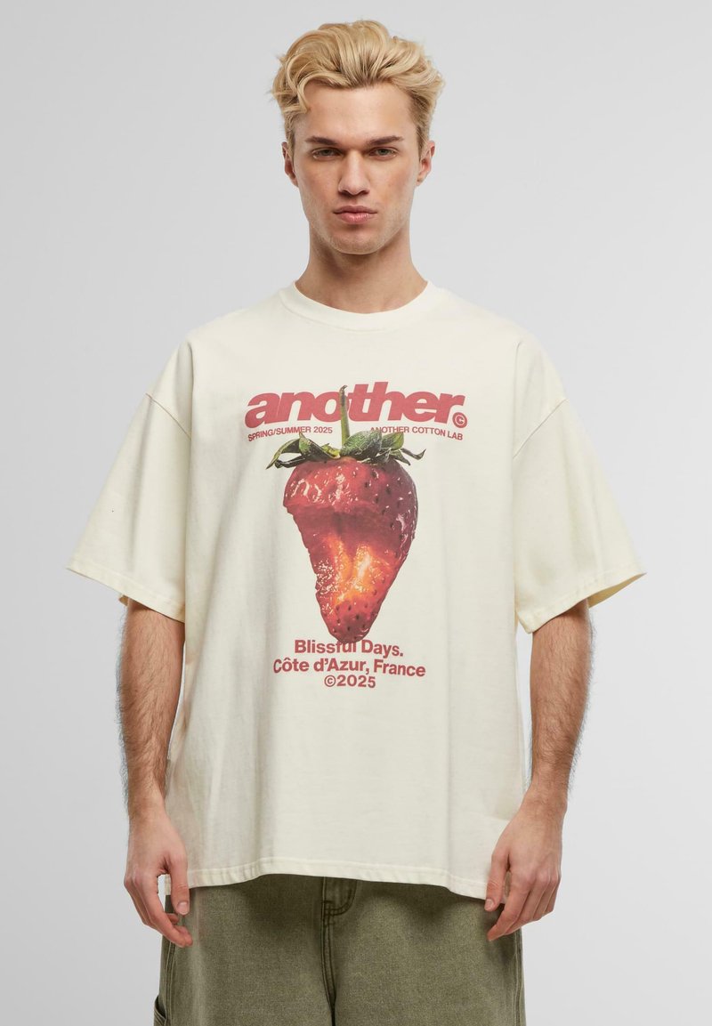 Cremefarvet oversized t-shirt lavet af bomuld, med et grafisk print af en jordbær og tekst i rød og sort. Korte ærmer.