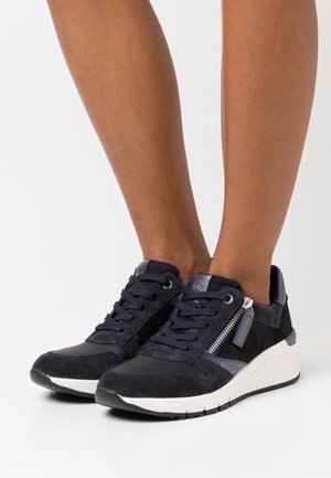 Marinblå mockaskor har en dragkedjedetalj, rund tå och en vit gummisula med texturerade detaljer för grepp och stöd.