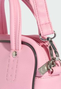 Ružová kožená kabelka s okrúhlym tvarom. Obsahuje strieborné kovanie, kontrastné stehy a zips s logom.