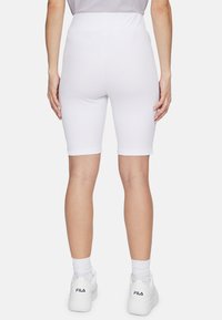 Shorts da ciclismo bianchi a coste con vita alta, che arrivano appena sopra il ginocchio, abbinati a sneaker bianche e calzini alla caviglia.