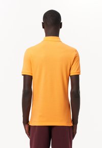 Orange kortärmad pikétröja med rak fåll och ribbad krage. Tyget är mjukt och något figursytt. Inga synliga logotyper eller mönster.