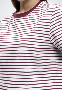 Ριγέ κοντομάνικη μπλούζα σε λευκό και βουργουνδί, με στρογγυλή λαιμόκοψη με βουργουνδί ρέλι και μαλακό, υφασμάτινο ύφασμα.