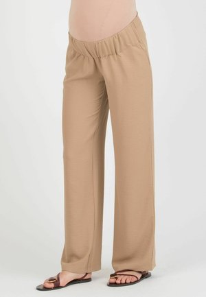 Beige løstsiddende bukser med elastisk linning båret med brune flade sandaler med guldbeslag.