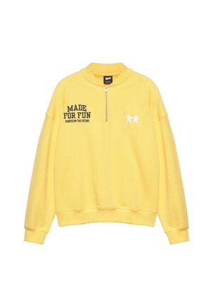 Gele sweater met lange mouwen en een rits aan de voorkant, zwarte tekst "MADE FOR FUN SHAPED BY THE FUTURE" op de linkerborst en twee kleine witte figuurtjes op de rechterborst.