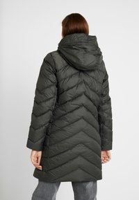 Quiltad mörkgrön vadderad jacka med huva, med sicksackmönster och långa ärmar. Inkluderar sidofickor och en mjuk textur.