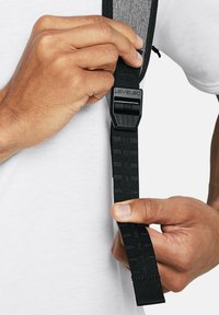 Cinghia nera regolabile con tessuto testurizzato e fibbia di plastica etichettata "LEVLED". Una mano afferra la cinghia su uno sfondo di camicia bianca.