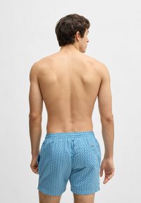 Blå mönstrade badshorts med geometrisk design, elastisk midja och sidofickor. Materialet verkar lätt och andas.