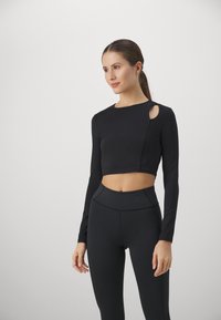 Black long-sleeve crop top with a side cutout, paired with high-waisted black leggings. Smooth texture with fitted design and seams.