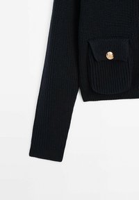 Pull en tricot noir avec une poche avant et un bouton doré, tissu texturé et poignets côtelés. Manches longues, design cropped.