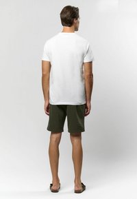 Bílý krátký rukáv tričko spárované s olivově zelenými šortkami, zobrazené zezadu, s plochými sandály a minimalistickým designem.