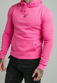 Rosa huvtröja i mjukt material, med en framficka, ribbade muddarna och en liten logotyp på bröstet.