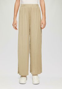 Beige Plisseehosen mit weitem Bein, ausgestattet mit einem elastischen Bund und glatter Textur, kombiniert mit weißen Sneakers.