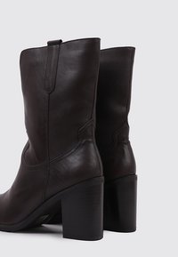 Brown leather ankle boots with a chunky heel, curved top line, and subtle stitching details on the sides. Smooth texture with minimal hardware.