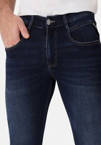 Dunkelblaue Denim-Jeans im klassischen Schnitt, mit einem Knopfverschluss, Fronttaschen und kontrastierenden Nähten. Glatte Textur und ausreichend Dehnbarkeit.