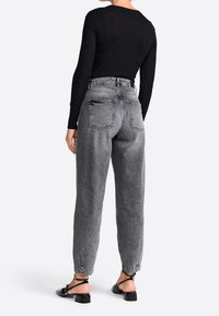 Hochgeschnittene graue Denim-Jeans mit einer lockeren Passform, ausgestattet mit Gesäßtaschen und umgeschlagenen Säumen, kombiniert mit einem schwarzen Langarmoberteil und Sandalen.