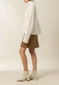Chunky Creme-Strickrollkragenpullover, brauner Kunstleder-Minirock und beigefarbene Lack-Ankle-Boots mit Blockabsatz und seitlichem Reißverschluss.