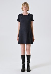 Marineblaues Kurzarmkleid mit tailliertem Oberteil, gef älteltem Rock, vorderen Knöpfen und glattem Stoff; kombiniert mit kniehohen schwarzen Lederstiefeln.