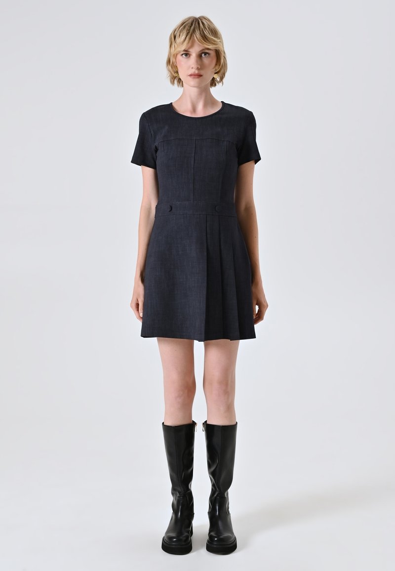 Marineblaues Kurzarmkleid mit tailliertem Oberteil, gefälteltem Rock, vorderen Knöpfen und glattem Stoff; kombiniert mit kniehohen schwarzen Lederstiefeln.