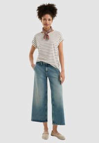 T-shirt a righe a maniche corte in crema e bordeaux, abbinato a jeans in denim scoloriti a gamba larga. Accessoriato con una sciarpa marrone a fantasia e scarpe intrecciate.