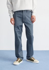 Pantalons en coton bleus à coupe droite, dotés d'une fermeture à bouton, de poches latérales et associés à des baskets beiges et vertes.