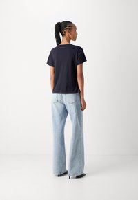 Marineblauwe katoenen t-shirt met korte mouwen, ruglogo-detail, gecombineerd met lichtblauwe wijde jeans en zwarte enkellaarsjes met hak.
