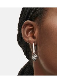Silberne Creole mit einem diamantenförmigen Anhänger, der ein Logo-Design zeigt, mit einem glänzenden Metallfinish und glatter Textur.