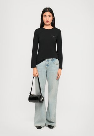 Black long-sleeve t-shirt with a logo on the chest, paired with light blue flared jeans and a round black handbag with white lettering.
