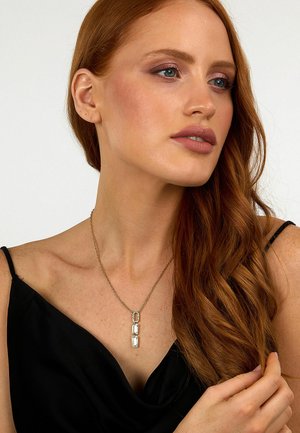 Collana in argento con tre pendenti rettangolari a finitura lucida, indossata sopra un top in satin nero con scollatura drappeggiata.